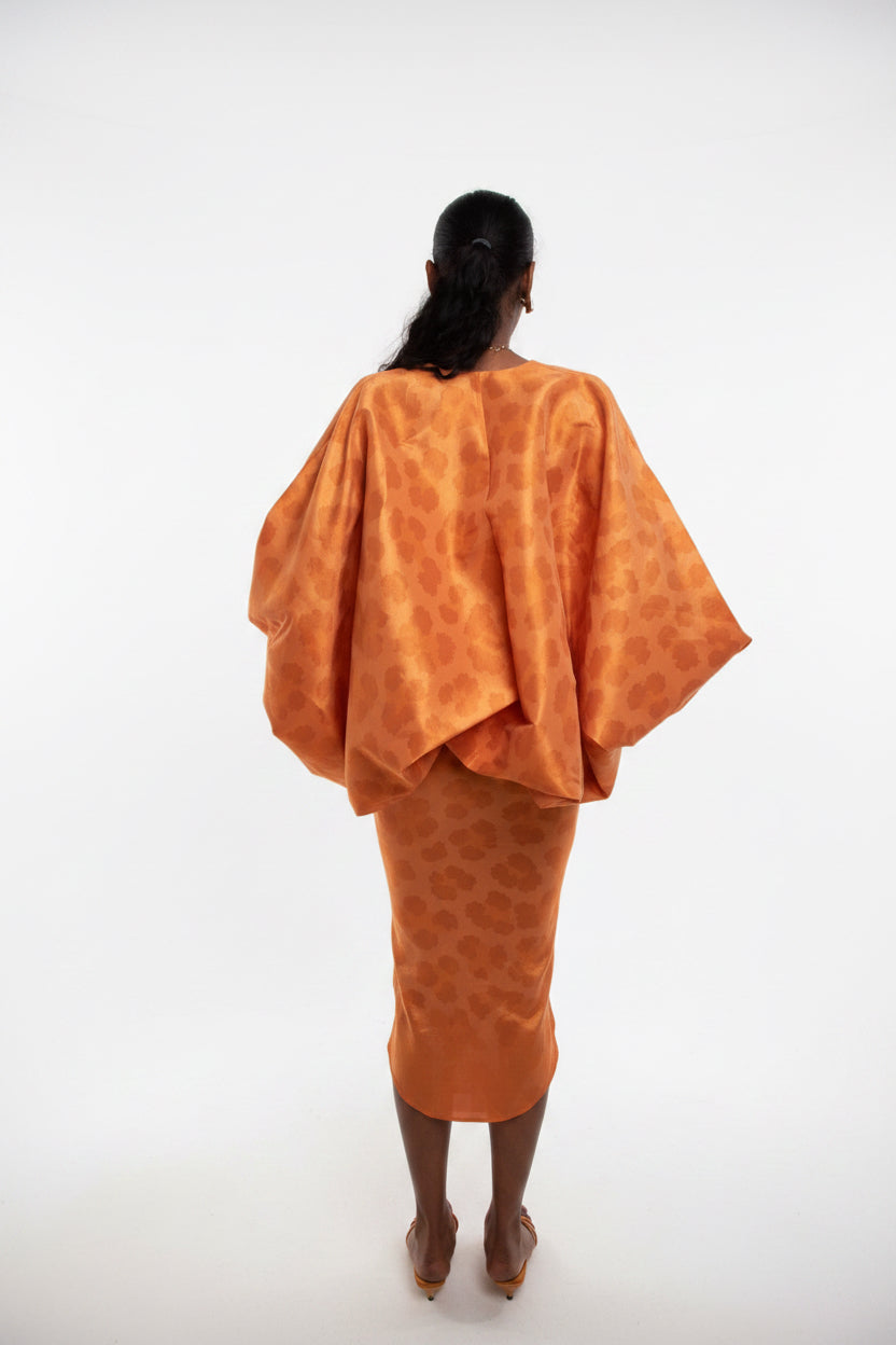 Person wearing an orange patterned outfit standing against a plain wall.